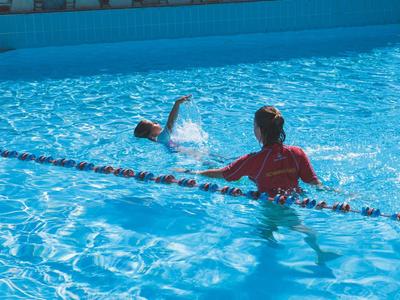 Dítě a dospělý plavou ve velkém slunném modrém bazénu.