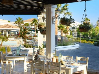 Restauranční terasa s bílými stoly a židlemi pod přístřeškem, zdobená závěsnými rostlinami.