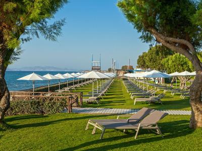 Grüner Rasen mit Liegestühlen und Sonnenschirmen am Wasser mit klarem Himmel.