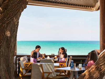 Lidé si povídají u stolu na terase s výhledem na moře.