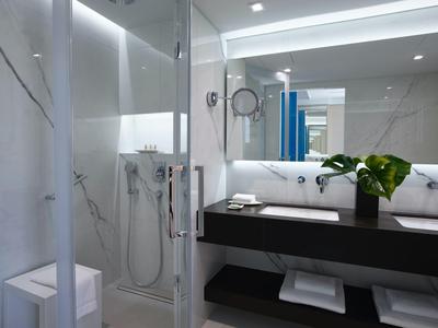 Moderní hotelová koupelna se skleněným sprchovým koutem a osvětleným zrcadlem.