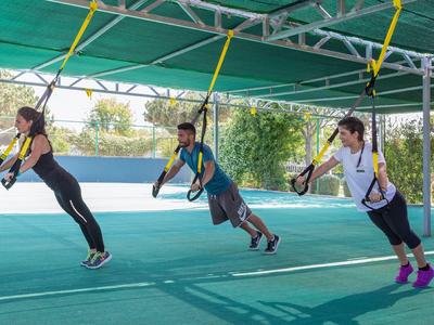 Drei Personen trainieren mit TRX-Bändern unter einem grün gedeckten Pavillon im Freien.