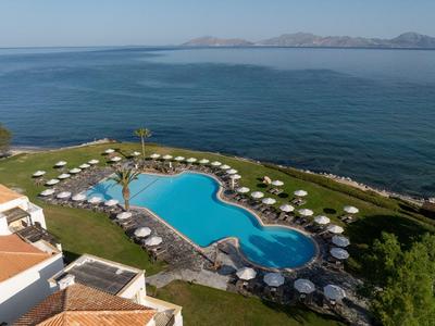 Blick auf einen Pool mit mehreren Sonnenschirmen und Blick auf das Meer im Hintergrund.