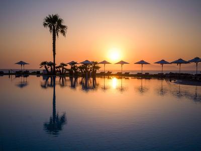 Sonnenuntergang über einem Pool mit Palmen und Sonnenschirmen am Wasser