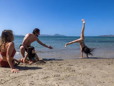 Čtyři lidé na pláži, jedna dělá kotrmelec, ostatní ji povzbuzují.