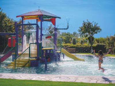 Dítě si hraje v aquaparku se skluzavkami a vodními atrakcemi za slunečného dne.