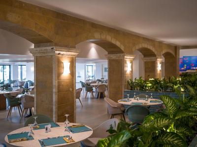 Elegantní restaurace s kamennými oblouky, prostřenými stoly a zelenými rostlinami.