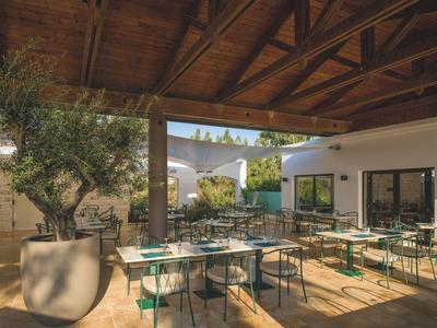 Krytá venkovní část hotelu s stoly, židlemi a dekorativními rostlinami.