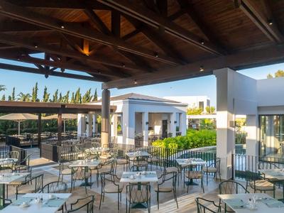 Venkovní terasa hotelové restaurace s stolem a židlemi pod dřevěnou střechou.