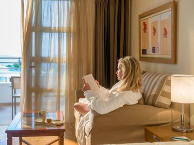 Žena v županu čte na pohovce u okna s výhledem na moře.