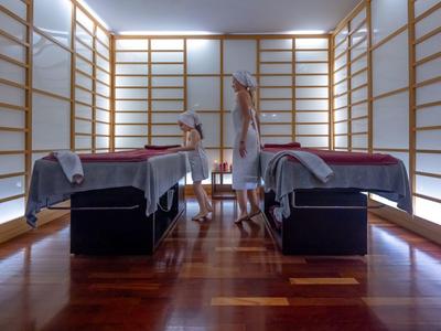 Moderní masážní místnost se dvěma lehátky a jemným osvětlením na dřevěné podlaze.