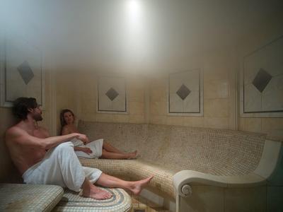 Dva lidé v županech odpočívají na velké pohovce ve spa nebo relaxační místnosti.