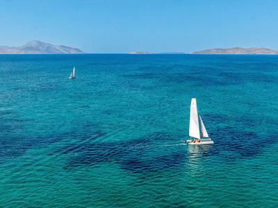 Segelboote fahren auf klarem türkisem Wasser mit Inseln am Horizont.