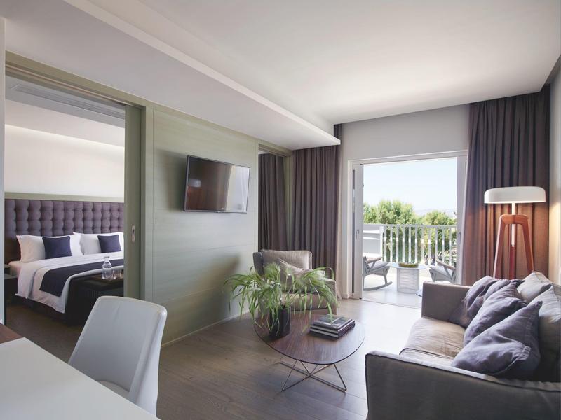 Světý obývací pokoj s pohovkou, křesly a dveřmi na balkon s výhledem do zeleně.