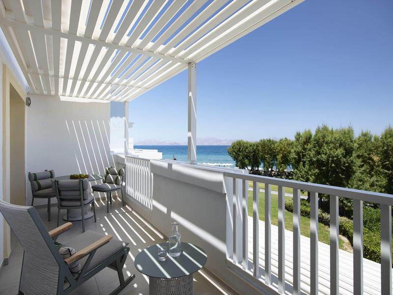 Hotelový balkon s křesly, výhledem na moře a jasnou oblohou.