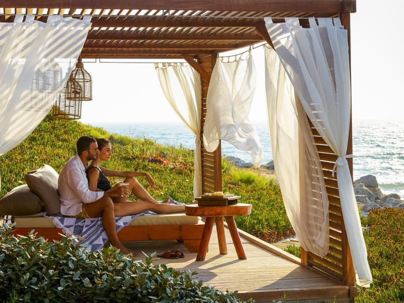 Pár odpočívající pod pergolou u moře s bílými zavěšenými závěsy.