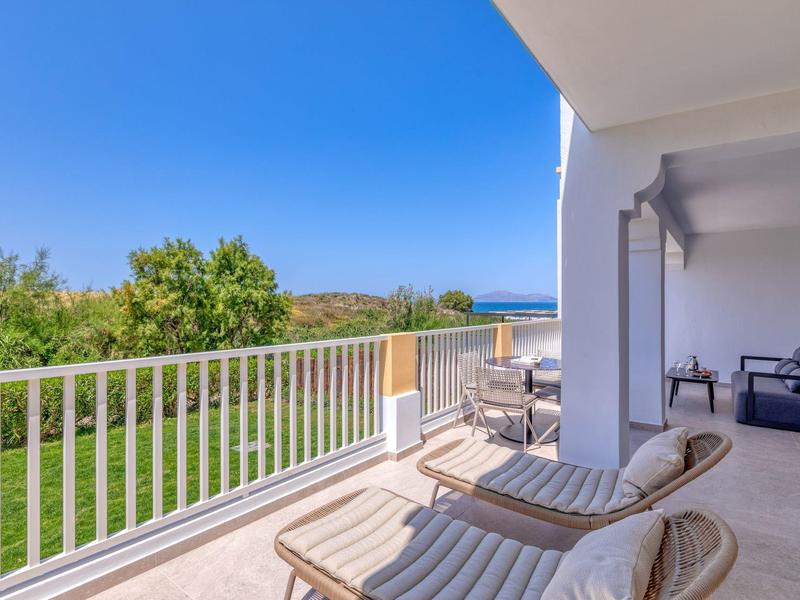 Terasa s lehátky s výhledem na zahradu a moře za jasné modré oblohy.