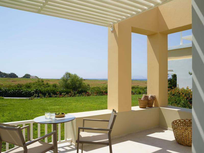 Terasa s židlemi a stolem s výhledem na zelenou zahradu pod jasnou oblohou.