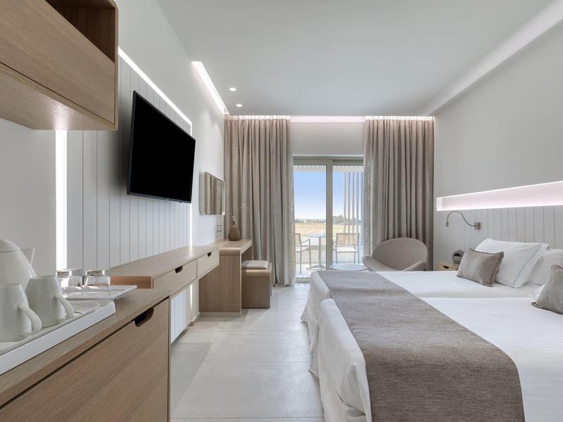 Moderní hotelový pokoj s dvojlůžkem, televizí na zdi a balkonem s výhledem na moře.
