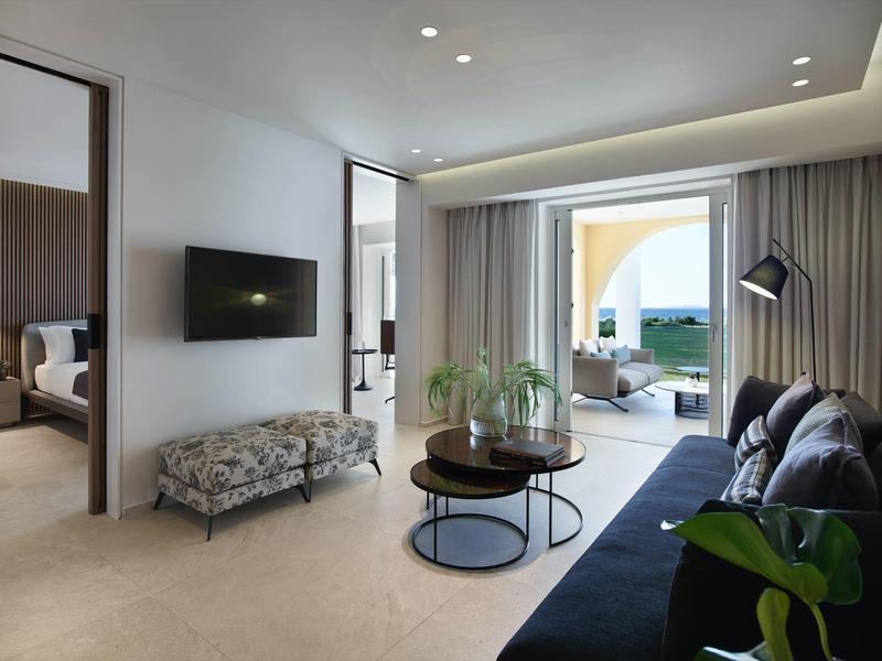 Moderní obývací pokoj s modrou pohovkou, kulatým stolkem, otevřeným oknem na terasu s výhledem na moře.