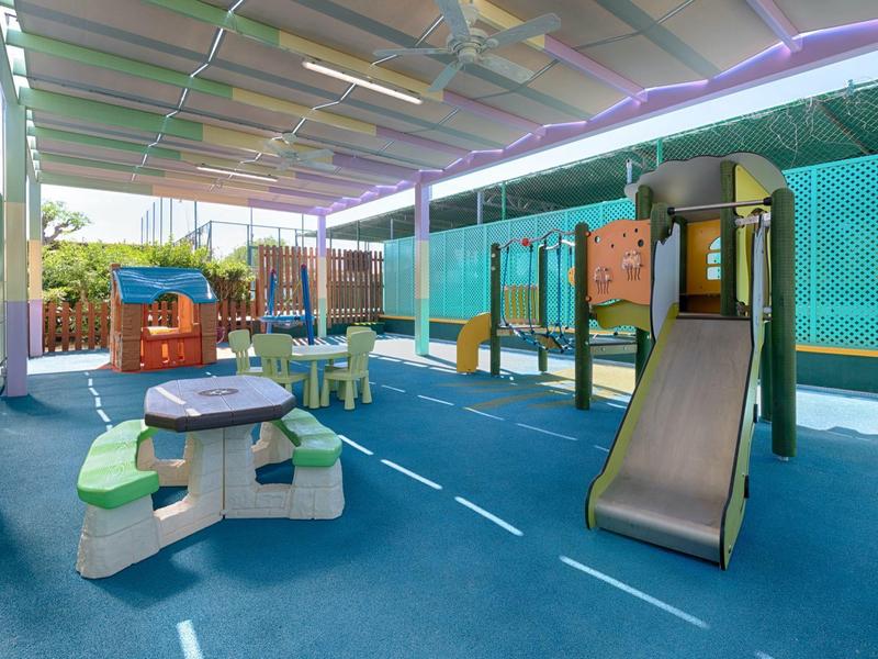 Barevné venkovní hřiště s klouzačkou a stoly pod částečnou střechou.