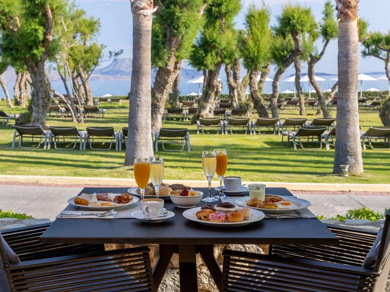 Stůl s snídaní na terase s výhledem na zahradu s palmami a moře v pozadí.