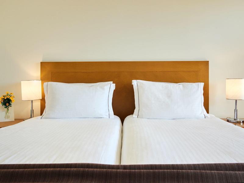 Hotelový pokoj se dvěma jednolůžky vedle sebe, bílým povlečením a tlumeným osvětlením.