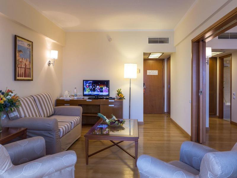 Hotelový pokoj s pohovkou, křesly, televizí a útulnou výzdobou.