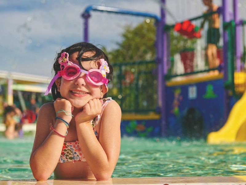 Šťastná dívka s růžovými plaveckými brýlemi odpočívá v bazénu v letovisku.