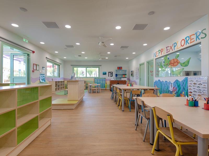 Světlá místnost s barevnými stoly, židlemi a policemi v přátelském prostoru pro děti.