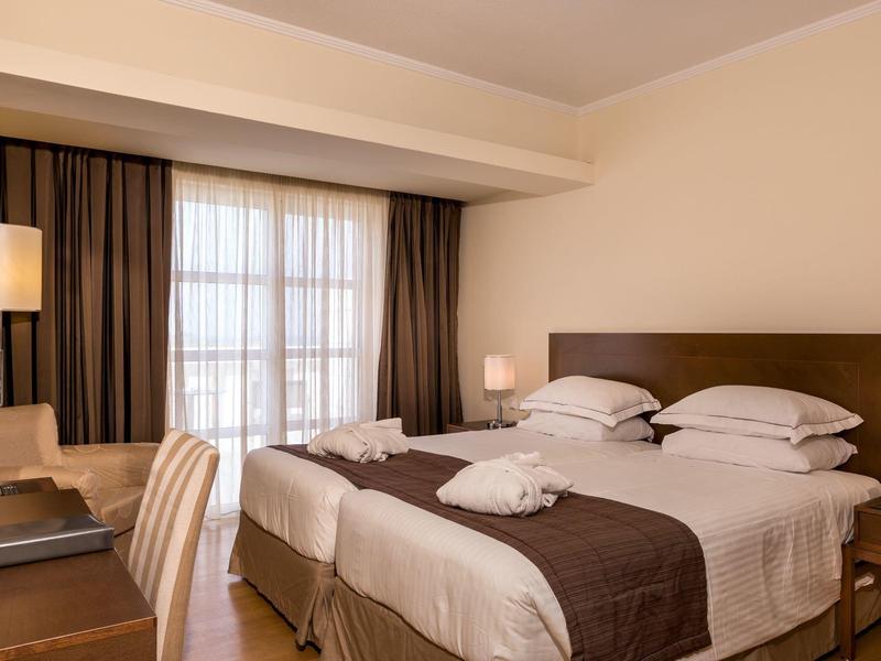 Hotelový pokoj se dvěma postelemi, hnědými závěsy a dřevěným stolem.