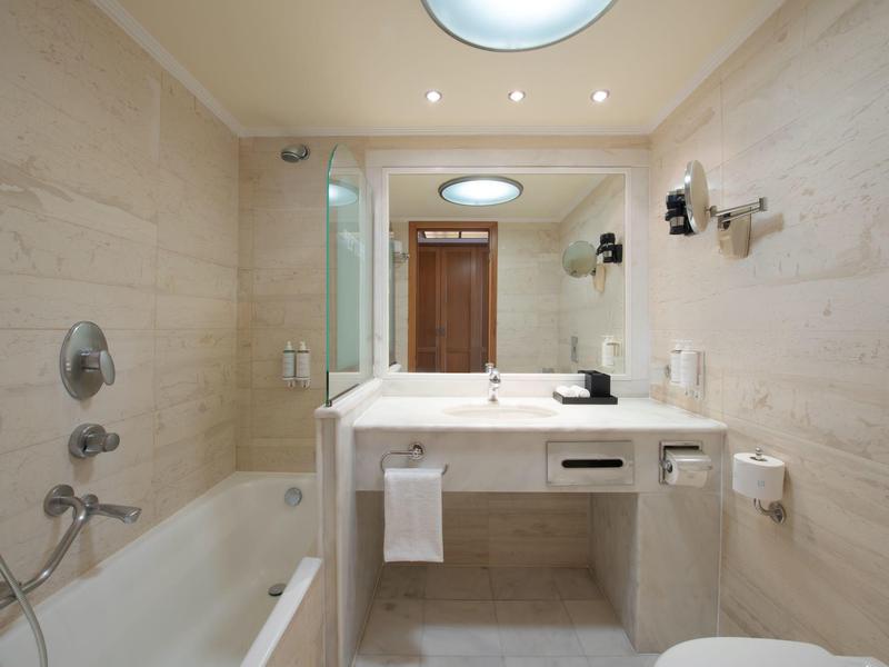 Moderní koupelna s vanou, dvojitým umyvadlem a osvětleným zrcadlem.