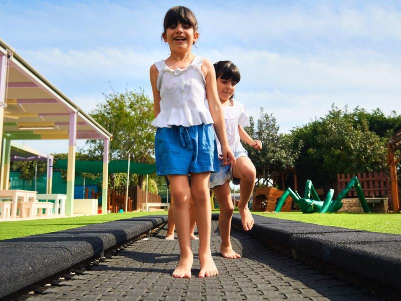 Veselé děti hrající si na trampolíně na slunečném hřišti.
