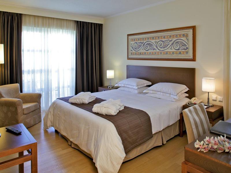 Hotelový pokoj s manželskou postelí, křeslem a přirozeným světlem z okna.