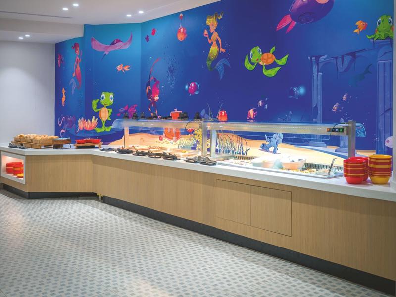 Bufetová část s jídlem a barevným podmořským dekorativním motivem na zdi v hotelu