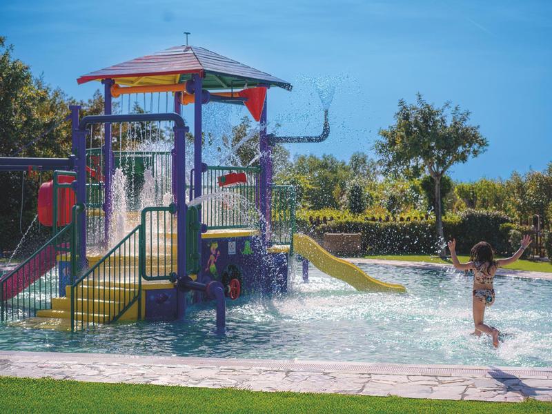 Dítě si hraje v aquaparku se skluzavkami a vodními atrakcemi za slunečného dne.