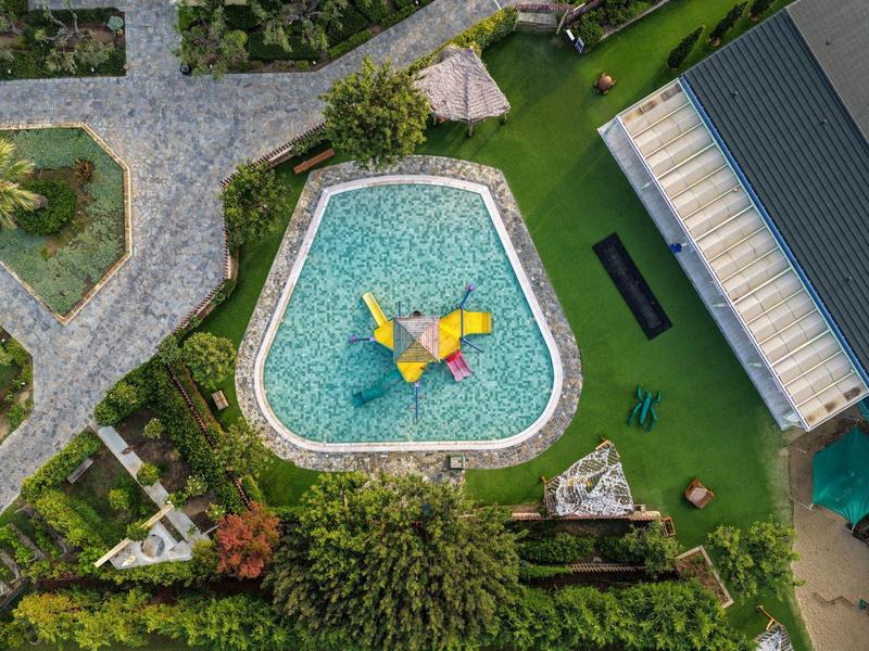 Letecký pohled na bazén ve tvaru srdce s vodními prvky a okolní zahradou.