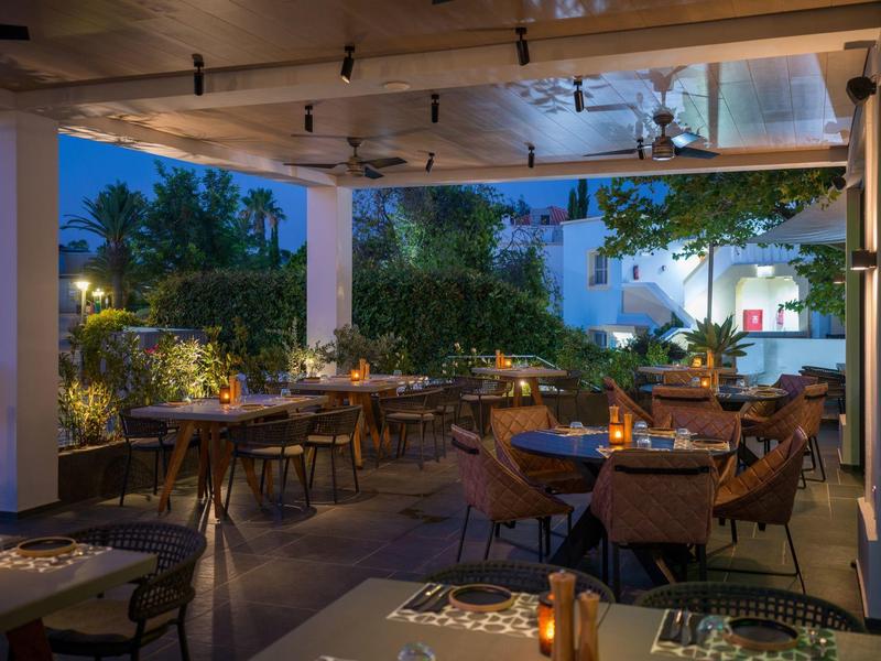 Elegantní restaurace na terase večer, dřevěné stoly a pohodlné židle pod otevřenou střechou.