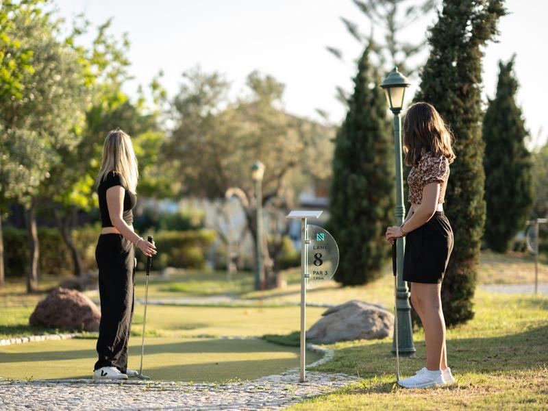 Dvě ženy hrají minigolf venku v zeleném parku.