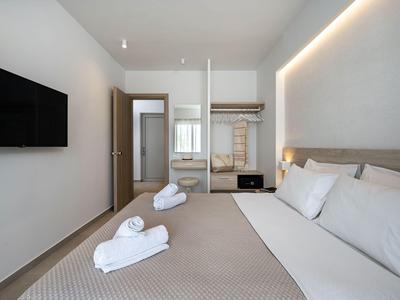 Camera d'hotel moderna con letto matrimoniale, TV a parete e appendiabiti aperto.