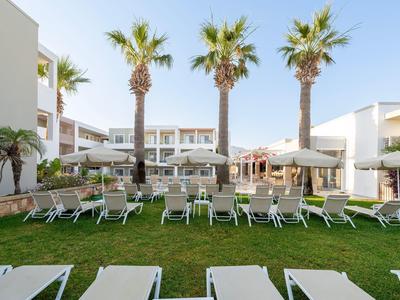 Sonnenliegen auf einem grünen Rasen mit Palmen und weißen Hotelgebäuden im Hintergrund