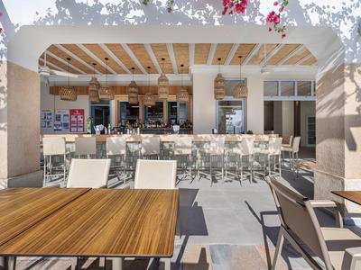 Area esterna moderna di un hotel con bar, tavoli e sedie al sole.