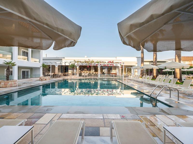 Moderner Poolbereich mit Sonnenschirmen und Liegestühlen vor einem Hotelgebäude bei Tageslicht