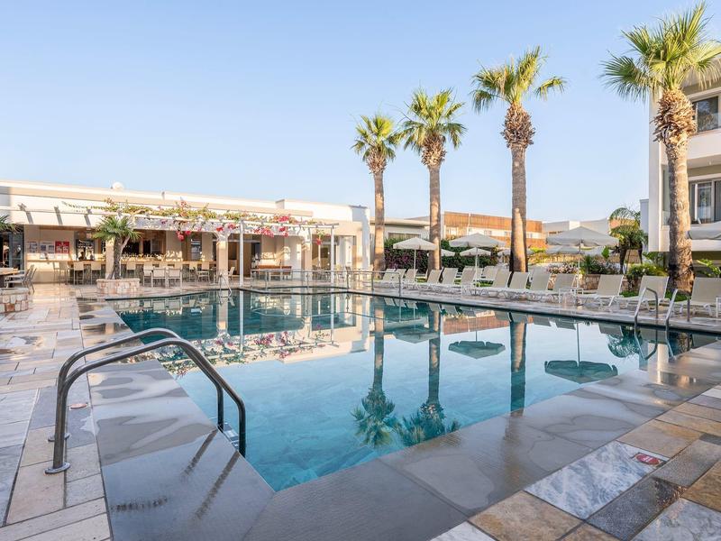 Moderner Hotelpool mit Sonnenliegen und Palmen bei klarem Himmel