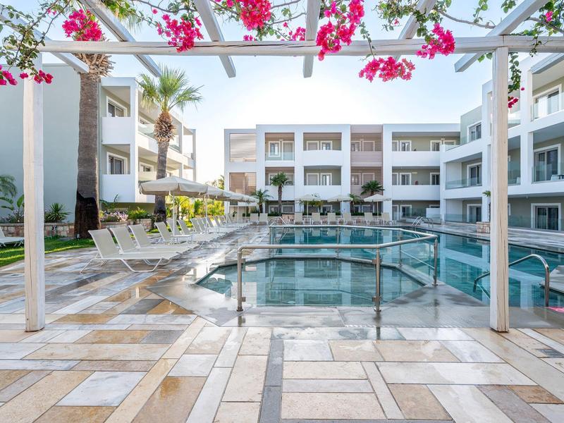 Moderner Hotelpool mit Liegestühlen und blühender Pergola bei sonnigem Wetter.