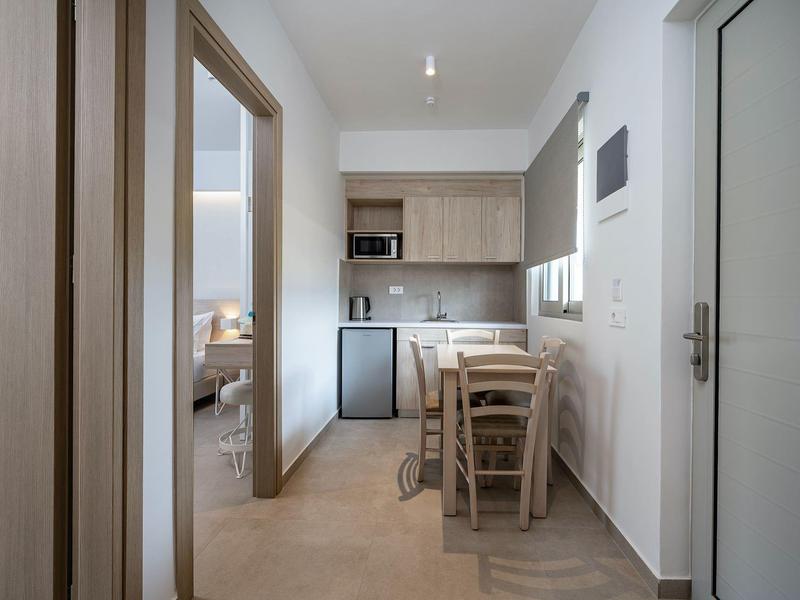 Kleine Küchenzeile mit Esstisch in einem Hotelzimmer, heller Raum mit Holzmöbeln.