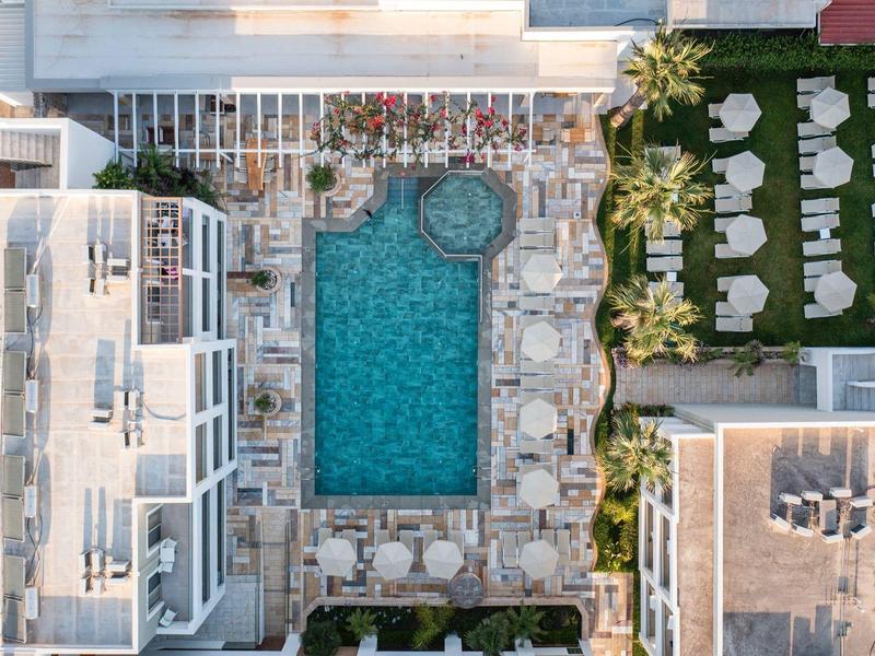 Vogelperspektive eines Hotels mit rechteckigem Pool und Sonnenliegen auf einer gepflasterten Terrasse
