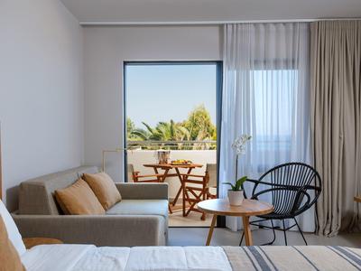 Modern hotel room with balcony, seating area, and greenery view.
