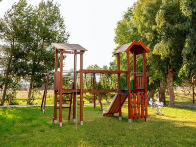 Play structure and swing set on a grassy area with trees in the background.