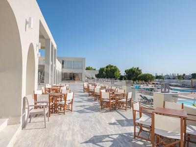Terrace with wooden tables and chairs beside pool under clear blue sky.